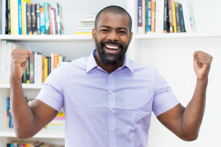Portrait of cheering african american businessman with beard indoors at officeの写真素材