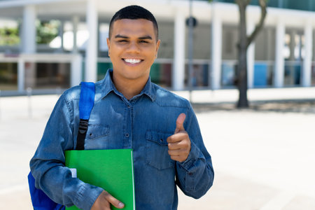 Mexican male student with backpack showing thumb up at campus of universityの写真素材