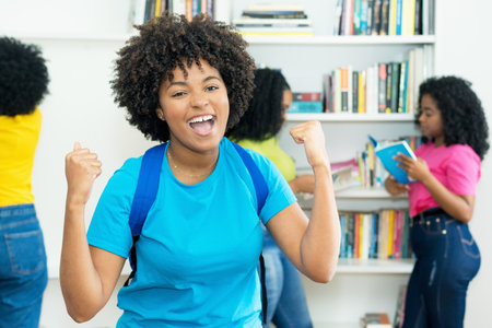 Cheering black female student with group of african american college students indoors at libraryの写真素材