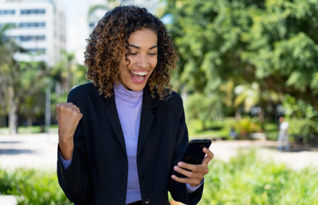 Successful mexican businesswoman receiving message with good news on phone outdoor in cityの写真素材
