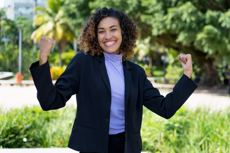 Cheering latin american businesswoman with blue blazer outdoor in city in summerの写真素材