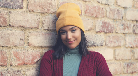 Smiling latin american young adult woman with bobble hat outdoor in city in winterの写真素材