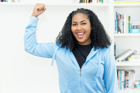 Successful cheering mexican woman with hoody indoors at homeの写真素材