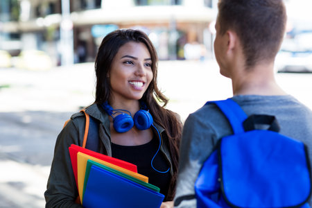 Laughing latin american female student talking with male student in city in summerの写真素材