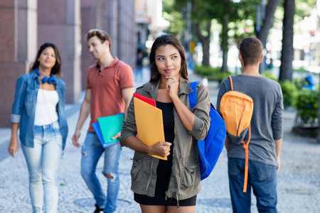 Pretty latin american young adult woman walking in city with group of students outdoors in cityの写真素材