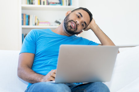 Latin american man streaming romantic movie online at computer indoors at homeの写真素材