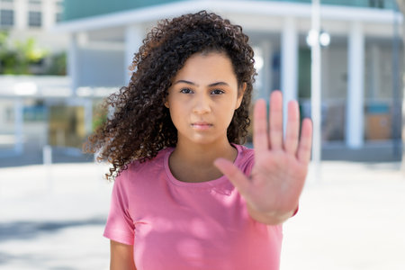 Hispanic feminist young adult woman gesturing stop outdoor in cityの写真素材