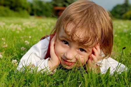 Little smiling girl lying on green grass in the garden summertime. See my other photos from this seriesの写真素材