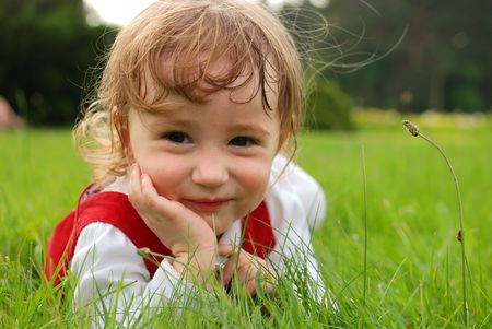 Little smiling girl lying on green grass in the garden summertime. See my other photos from this seriesの写真素材