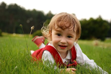 Little smiling girl lying on green grass in the garden summertime. See my other photos from this seriesの写真素材
