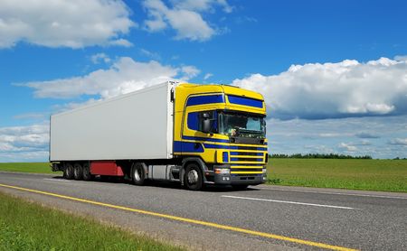 Truck (blue-yellow cabin) and white trailer moving on highway over bright sky. See my portfolio for additional beautiful vans and lorries.の写真素材