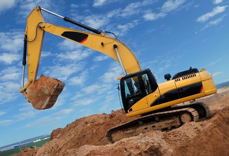 Excavator standing in sandpit with raised bucket full of sand over cloudscape skyの写真素材