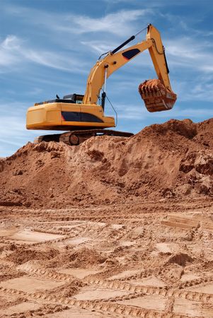 Excavator bulldozer in sandpit with raised bucket filled of sand over blue cloudscape skyの写真素材