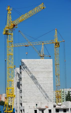 Group of yellow tower cranes building a house over blue skyの写真素材