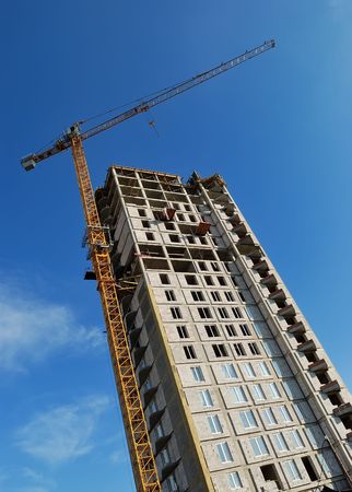 High yellow tower crane builds a multistory (multistoried building) over blue sky. Lower point of view.の写真素材