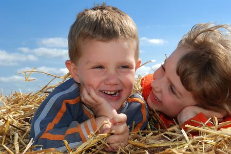 Smiling Boy and girl laying on the straw outdoors over blue skyの写真素材