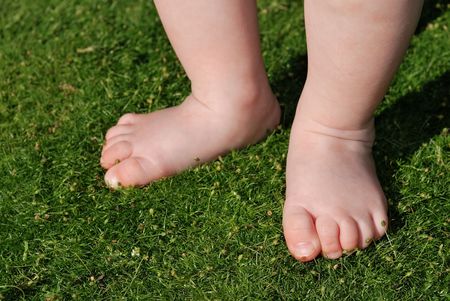feet of little baby staying on green grass outdoorsの写真素材