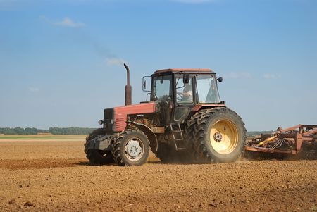Agriculture tractor in yellow field outdoors in summer with ploughの写真素材