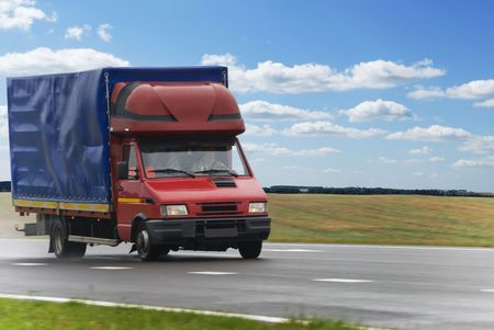 single red middle delivery truck moving on highway over blue cloudy skyの写真素材