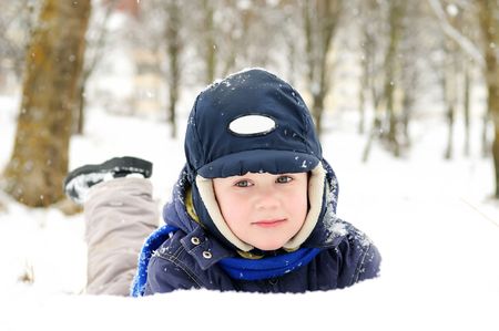 little boy lying in snow at winter outdoorsの写真素材