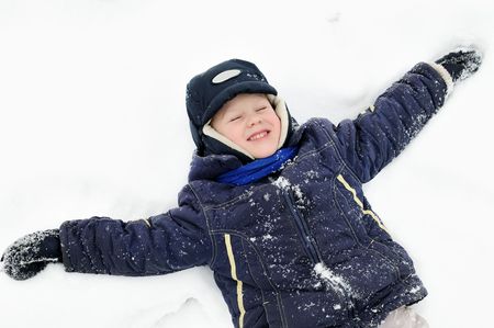 little boy lying in snow at winter outdoorsの写真素材