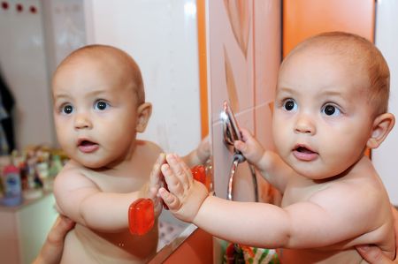 Little Baby standing against the mirror and looking at the reflectionの写真素材
