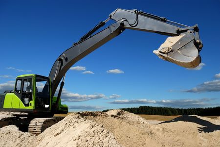 Excavator loader standing in sandpit with raised bucket over cloudscape skyの写真素材