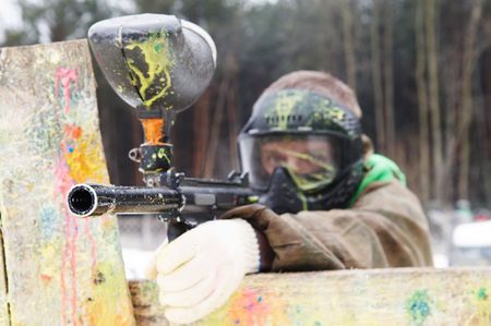 paintball sport player with mask aiming gun and shooting to enemy in winterの写真素材