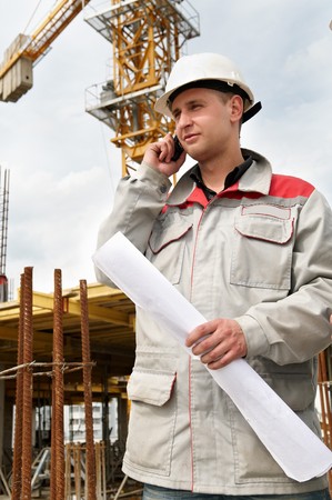 One happy engineer builder with blueprint at construction site speaking on mobile phone