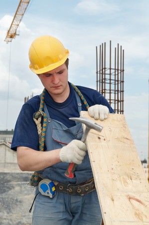 Worker builder at construction site working with plywood board and hammer