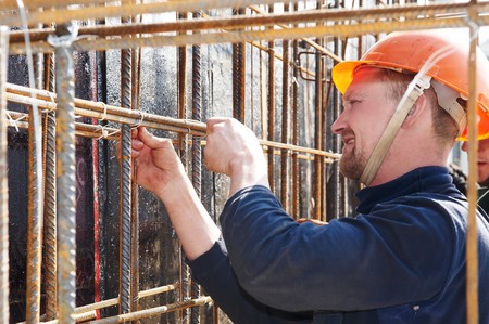 worker in helmet making metal mesh at construction site for concrete pouring