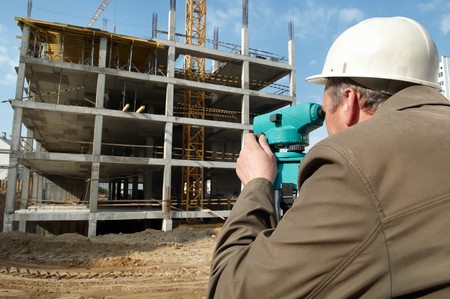 worker surveyor measuring distances, elevations and directions on construction site by theodolite level transit equipmentの写真素材