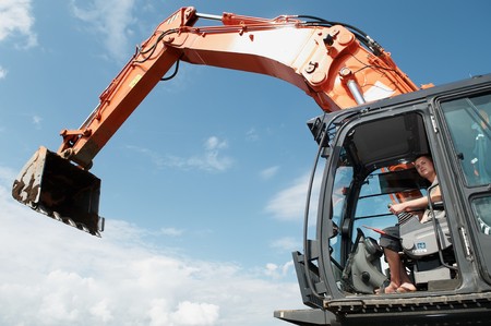 Loader Excavator doing construction works standing in field with risen bucket outdoors