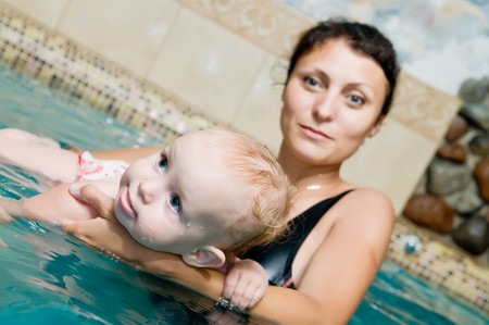 Mother and baby child playing in a swimming pool. Focus on baby face with mother defocused in the background.の写真素材