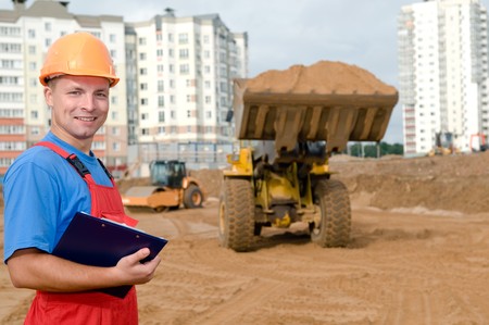 One smiley builder worker with clipboard inspecting earthmoving works at construction site