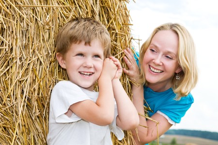 Happy playing mother with son in summer at field and straw haystackの写真素材