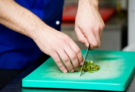 closeup hands of chef with knife cutting an greens on board in kitchenの写真素材