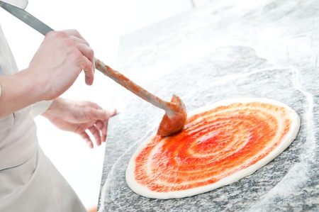 Closeup hand of chef baker in white uniform making pizza at kitchenの写真素材