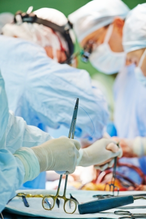 Hand with surgery foreceps in front of surgeons perfoming operation on a patient at cardiac surgery clinicの写真素材