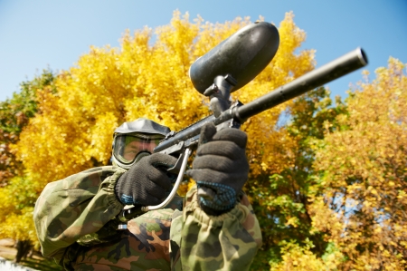 paintball sport player in protective uniform and mask aiming gun before shooting in summerの写真素材
