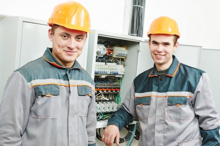 Happy young adult electrician builder engineer workers in front of fuseboardの写真素材