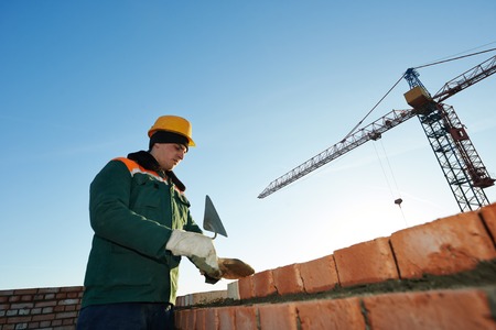 construction mason worker bricklayer installing red brick with trowel putty knife outdoors