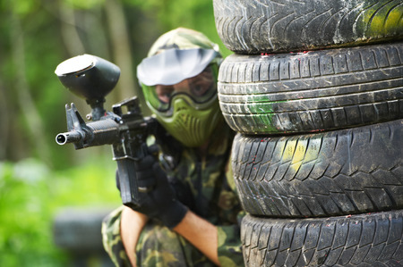 paintball player in protective uniform and mask aiming marker gun in summerの写真素材