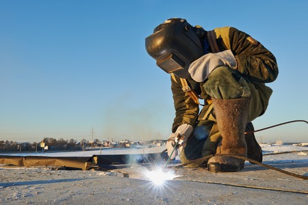 welder working with electrode at arc welding in construction site winter outdoors