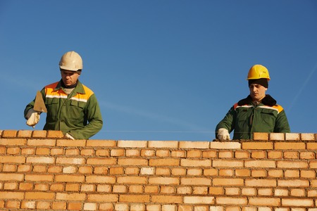 two construction mason worker bricklayer installing red brick with trowel putty knife outdoors