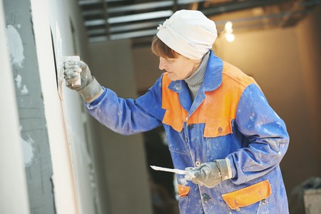 Plasterer at indoor wall renovation stucco decoration with float and plaster