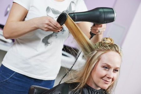 hairdresser drying hair with blow dryer of woman client at beauty parlour after highlightingの写真素材