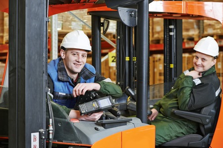 two young workers men in uniform at warehouse with forklift facilitiesの写真素材