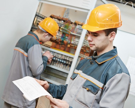 two electrician builder engineer with blue print scheme project in front of fuse switch box
