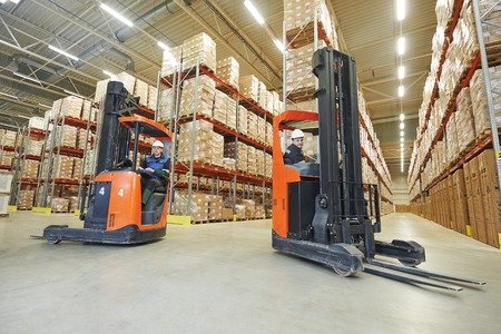 two young workers men in uniform at warehouse with forklift facilities